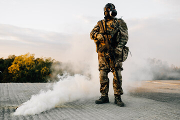 Soldier man standing on concrete in a gas mask next to a detonated smoke grenade on the street