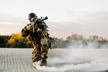 Military man in a gas mask sitting on concrete shooting at a target with a rifle