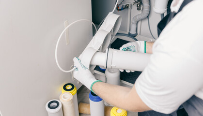 Plumber working install new cartridge for cold water filter in white kitchen