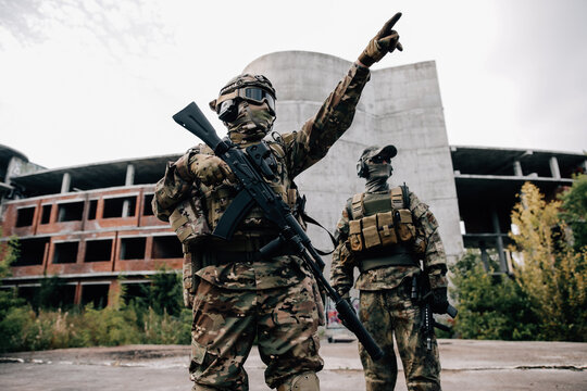 Two soldiers in camouflage uniforms with rifles in front of a building