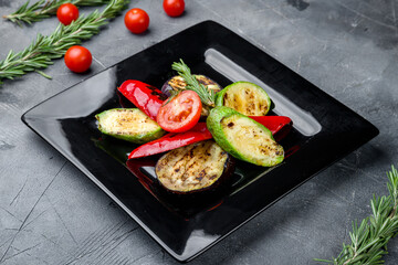 grilled vegetables on a black plate on grey table