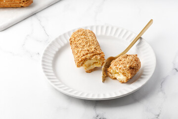 Cut Dessert vanilla eclair with cream with fork on white plate on marble background