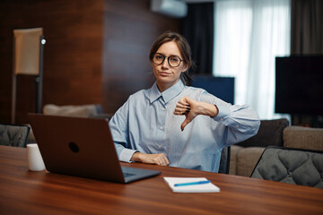 Upset business woman in glasses sit at laptop, showing dislike with thumb down, negative feedback, rejection concept - obrazy, fototapety, plakaty