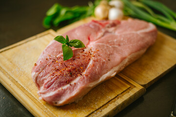 Chuleta de cerdo fresca sobre tabla de madera, decorada con albahaca