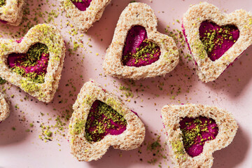 valentine's heart shaped sandwiches with beets and pistachios on a pink background with a cocktail