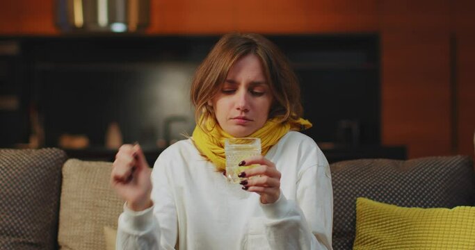 Sick female dissolve medicine tablet in water take medication to relive flu, fever symptoms, high temperature on sofa