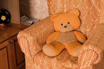 Old sad faced teddy bear sitting alone on armchair in living room. Depicts loneliness and...