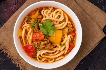 Lagman asian soup with meat, vegetables and noodles, dark table, uzbek cuisine top view