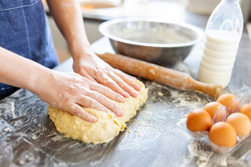 Female hands making dough for baking on wooden table near rolling pin, eggs and milk bottle. Culinary, cooking, baking concept