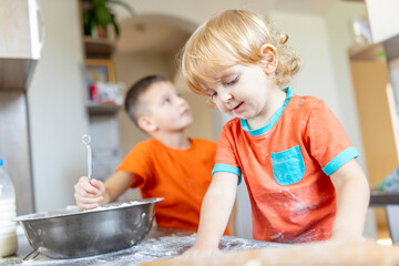 Two little cheerful boys prepare dough for the bread or pie in the kitchen