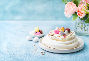 Easter cake. Meringue nest cake Pavlova with colorful chocolate eggs, buttercream frosting, light blue background. Selective focus.