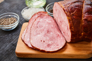 Homemade ham, sliced on a wooden table on a cutting board with spices and salt. Traditional ham homemade, ready to eat, delicious breakfast. The concept of meat products.