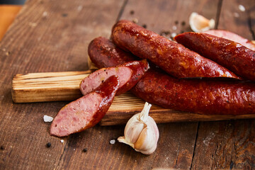 Homemade sausage with garlic cut into slices lies on a wooden table on a cutting board with spices and garlic. Traditional sausage, ready to eat, delicious breakfast. 