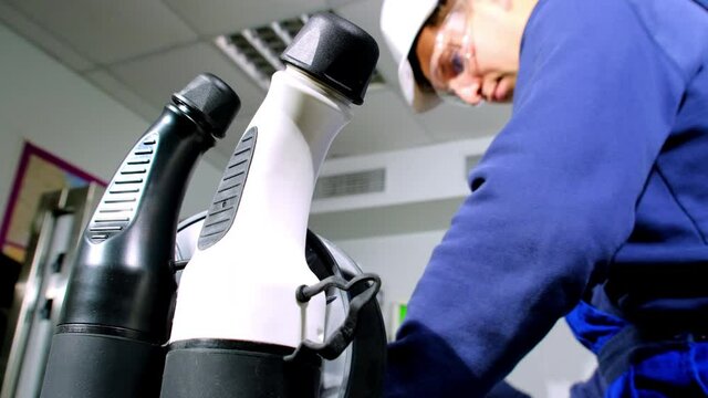 Portable charging station and worker. Experienced engineer in blue uniform and protective helmet prepares cables for plug in workshop
