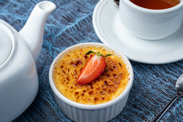 classic dessert creme brulee with strawberry on blue table with tea