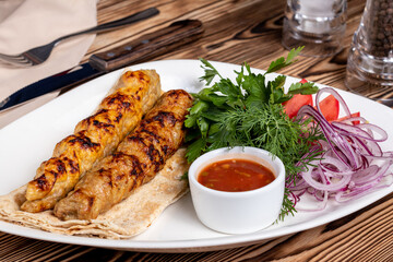 Lula kebab chicken with red onion and sauce on white plate