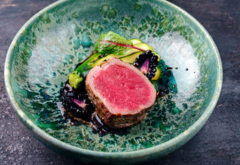 Modern style traditional fried dry aged angus beef filet medaillons natural with baby zucchini, lettuce and forest berries served as close-up on a design bowl