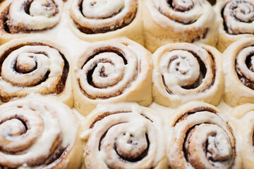 Freshly sweet baked cinnabon buns with cream chees sauce on baking paper. homemade rolls with Cinnabon cinnamon. Selective focus. French buns swirl, snail with glaze with cinnamon and cream