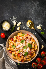 Italian pasta alla arrabiata with basil and parmesan cheese on dark table. Fusilli pasta with tomato sauce arrabbiata. Top view.