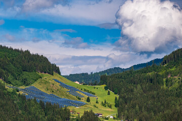 Photovoltaic, solar panels with alpine mountains in the background. Solar panels in country landscape over summer Alps is the innovation for sustainability of world solar energy. - obrazy, fototapety, plakaty