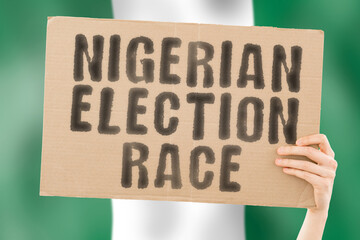 The phrase " Nigerian election race " on a banner in men's hand with blurred Nigerian flag on the background. Ballot box.  Politics. Conflict. Politic. Primary. Selection. Choosing. Onitsha