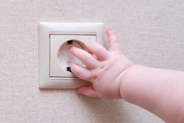 Baby toddler reaches into the electrical outlet on the home wall with his hand. Danger and...