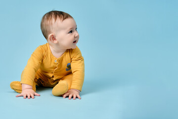 Naklejka premium Happy toddler baby sits on studio blue background. Funny child boy with a smile on his face, copy space