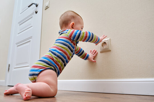 Baby Toddler Reaches Into The Electrical Outlet On The Home Wall With His Hand. Danger And Protection Of Child Fingers From Electric Shock