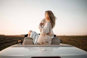 Happy woman sitting in white convertible car with beautiful view