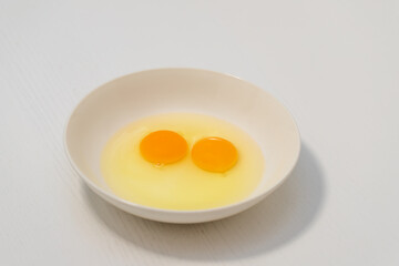 Two raw chicken eggs on on a white plate. Two raw egg yolks in a plate and around it is white.