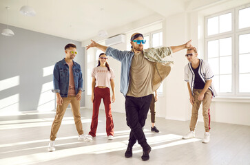 Happy diverse dancers have fun train together in bright studio. Funny male with young people crew or group dance prepare for contest indoors. Performance and entertainment, hobby concept.