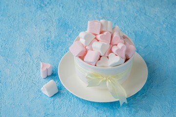 Pink and white marshmallow hearts in a white ceramic bowl on a blue concrete background. Valentine's day concept.
