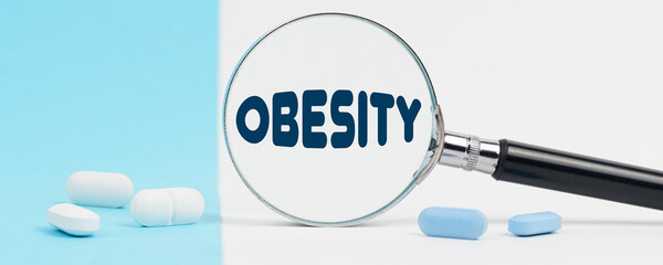 On a blue and white background, there are pills and a magnifying glass, inside of which it is written - OBESITY