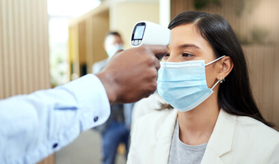 Naklejka premium Let's take your temperature. Cropped shot of an attractive young businesswoman wearing a mask and having her temperature taken while standing at the head of a queue in her office.