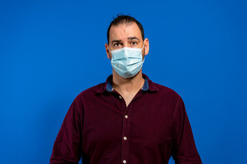 Portrait of handsome man with surgical medical mask standing, looking at camera with smile. indoor studio shoot, isolated on blue background