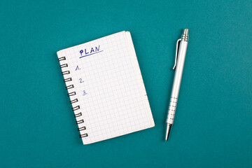 Empty notebook with a pen on a petrol colored background, the word plan is standing on the top of the page, planning new goals, to do list