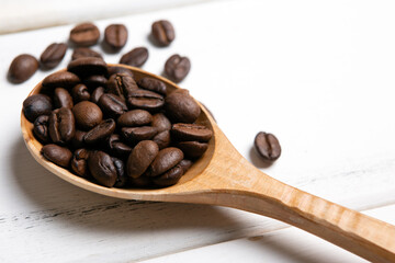 Obraz premium roasted coffee beans with wooden spoon on a white wooden background top view