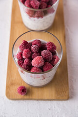 Dessert of yogurt, chia seeds, frozen raspberries in a glass, spoon, bowl with raspberries pink background, close-up