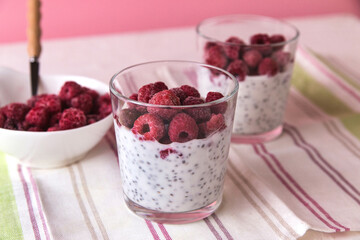 Dessert of yogurt, chia seeds, frozen raspberries in two glasses, bowl with raspberries pink background, close-up