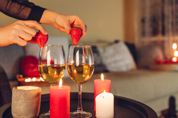 Woman decorates table setting for Valentines day celebration at home putting strawberries on wine glasses by candles