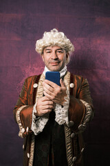 Adult man in classical medieval clothing using a mobile phone while standing on an isolated background.