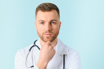 Portrait young bearded doctor with stethoscope over neck in medical coat standing against isolated blue background.