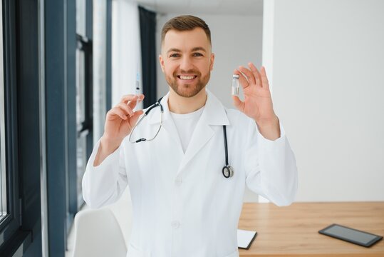 Doctor In PPE Holding A Vial Or Bottle Vaccine Against Coronavirus Covid 19 New Omicron Variant Or Strain In His Hand, Close Up. Concept Of Vaccination, Trial And Treatment Due To SARS-CoV-2 Pandemic