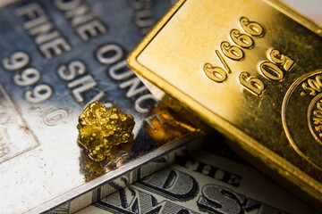 Close-up of a gold ingot and gold nugget on top of a troy ounce silver and US banknotes