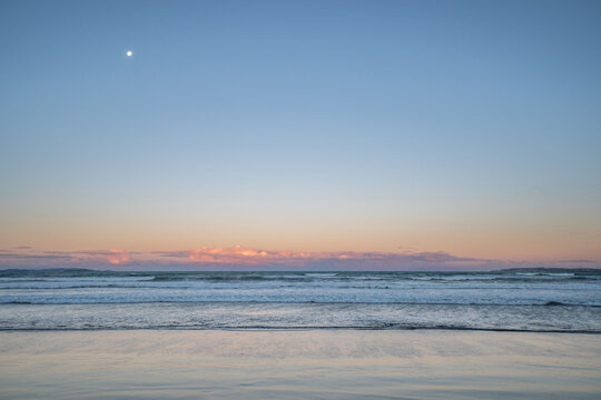 Beach Sunset Over the Waves at Orewa, Auckland New Zealand with Moon in the Sky
