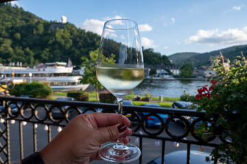 Hand holding glass of white quality riesling wine served on outdoor terrace in Mosel wine region...