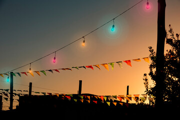 A set of multicolored pennants hanging above the backyard of a home with a dramatic sunset sky as the background.
