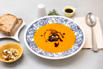 Fresh pumpkin cream soup on the plate with hazelnuts and pumpkin oil, served with fresh bread.  Ready to eat butternut squash soup on neutral background. Vegan food.
