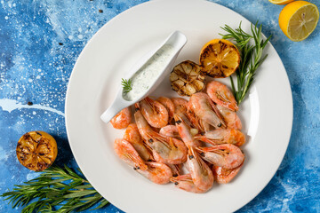 Pink shrimps with lemon on a blue abstract background. Healthy nutrition concept. Mediterranean diet, delicacies. Flat lay.