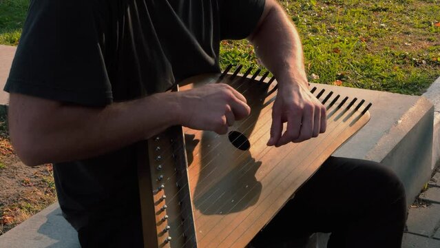 Musician hands beat the strings rhythmically. A man holds gusli on his lap and plays. Soft daylight. Close-up.